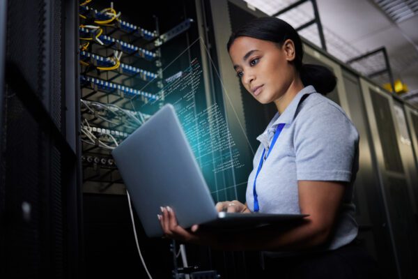 Professional security operator or system administrator working in server room with a laptop